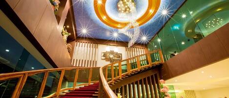 A modern hotel interior with a grand staircase, a decorative ceiling, and a view of the lobby area.