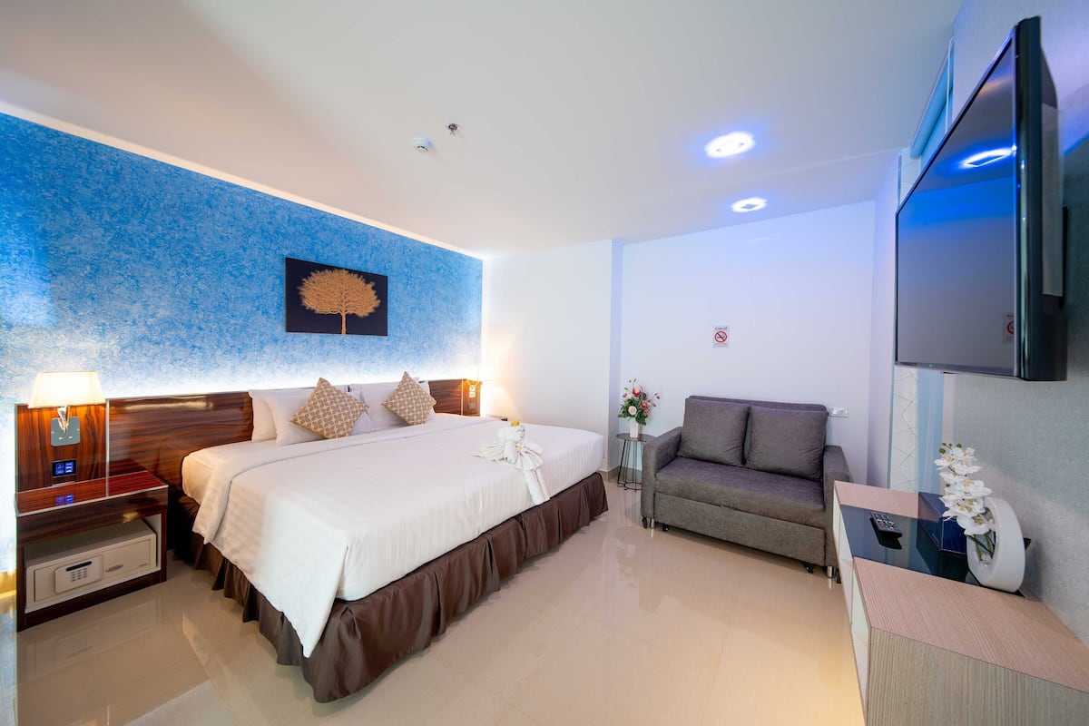 Ein modernes Hotelzimmer mit einem großen Bett, einer Couch, einem Fernseher und einem Schreibtisch mit Blumen.