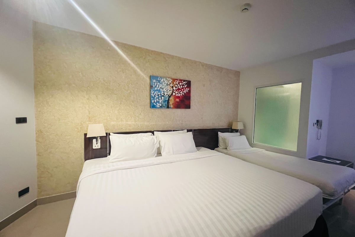 Ein Hotelzimmer mit einem großen Bett, einem Nachttisch mit Lampe, einem Gemälde an der Wand und einem Fenster mit Jalousien.