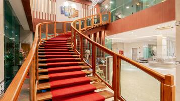 A grand staircase with a red carpet, wooden handrails, and a modern ceiling design with a chandelier.