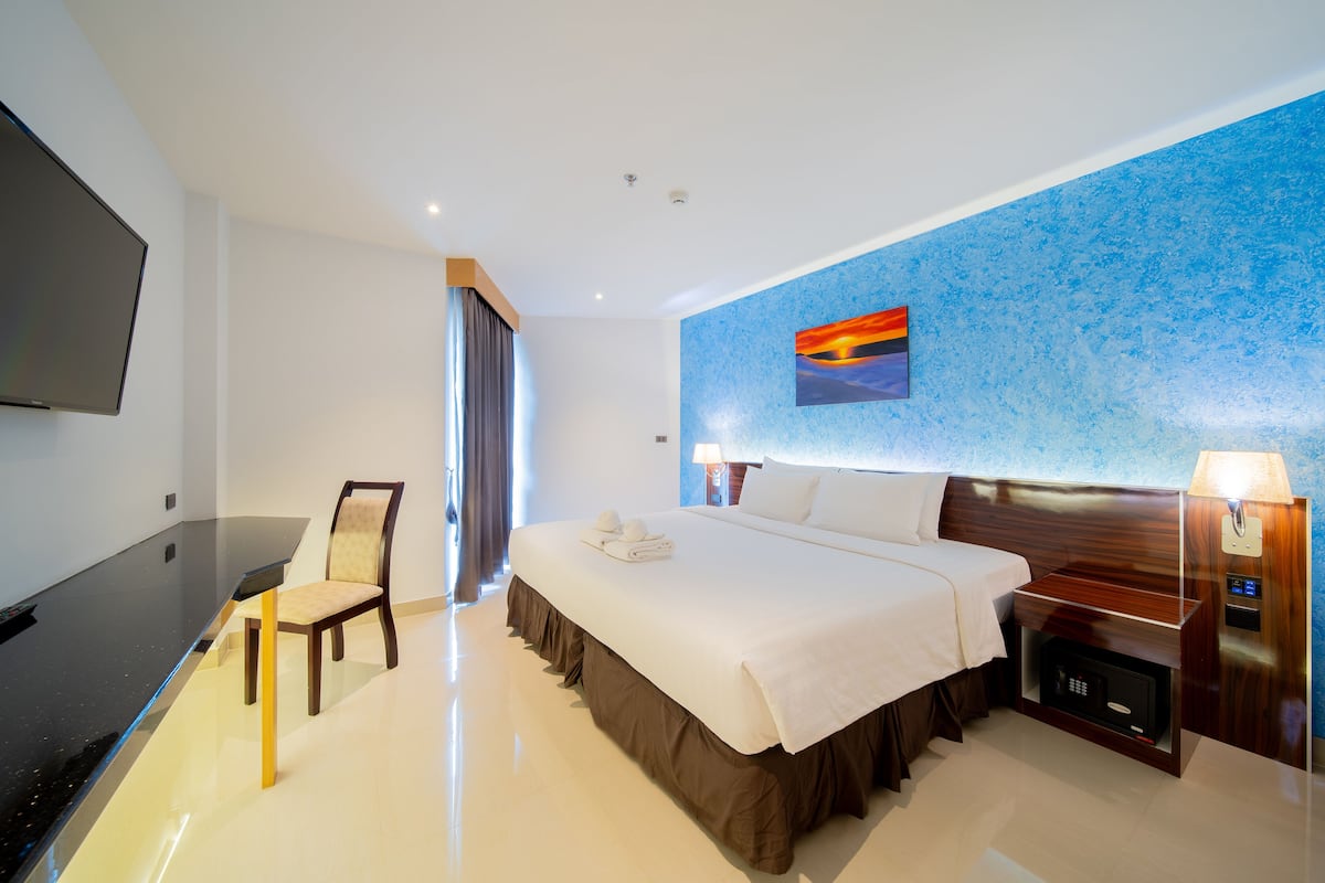 Ein Hotelzimmer mit Bett, Schreibtisch, Sessel, Fernseher und einem Wandbild.