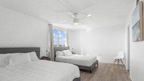 A modern bedroom with two beds, a ceiling fan, and a view of the outdoors. - Bay Harbor Sunset Apt 5C (Bay Harbor Islands)