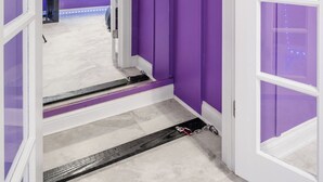 Un pasillo con paredes moradas y detalles blancos que conduce a una habitación con ventilador de techo y ventana con persianas.
