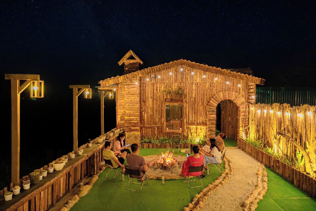 A rustic wooden building with a fire pit in the center, surrounded by people sitting on chairs.