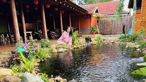 A serene outdoor area with a small pond, surrounded by rocks and various plants. - Gió Homestay – Măng Đen (Mang Den)