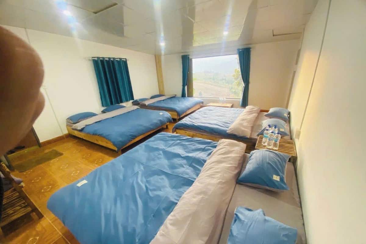 A room with four beds arranged in a row, a wooden floor, and a window with curtains.