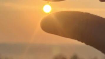 Una mano con le dita leggermente divarte che tiene un sole luminoso in basso nel cielo.