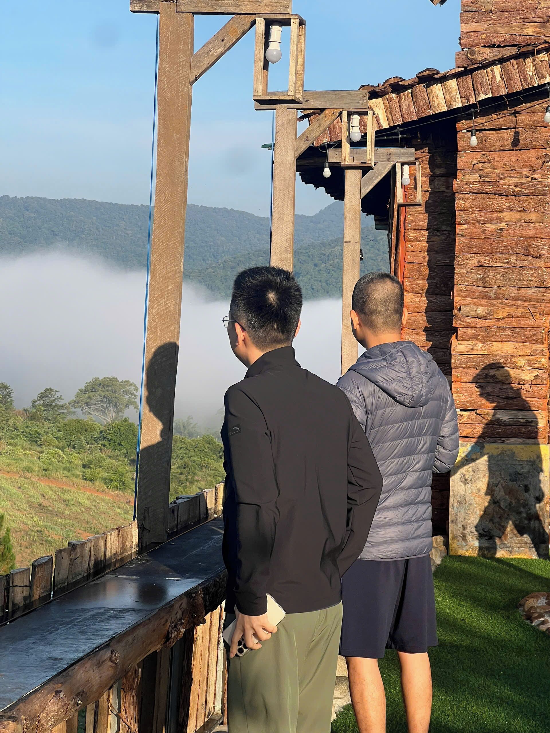 Two individuals standing on a wooden deck overlooking a mist-covered landscape.