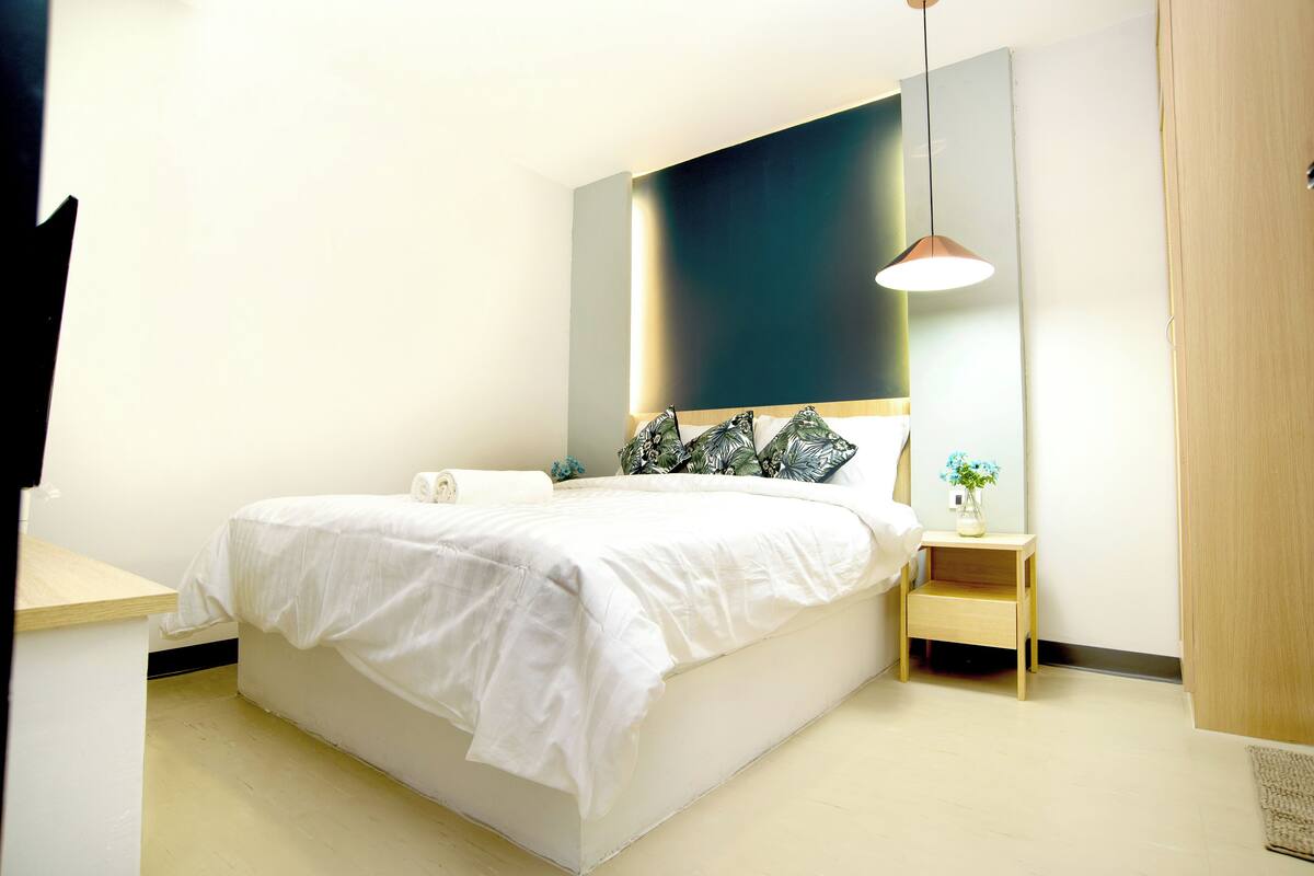 A modern bedroom with a large bed, bedside tables, a nightstand, and a hanging light fixture.
