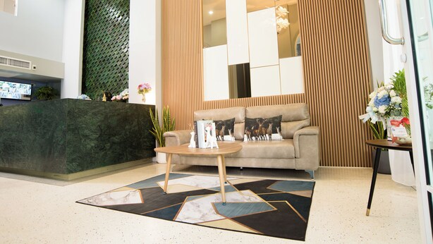 Un área de recepción con pared verde texturizada, un sofá beige con cojines de motivos animales, una mesa de centro y una mesita auxiliar con flores.