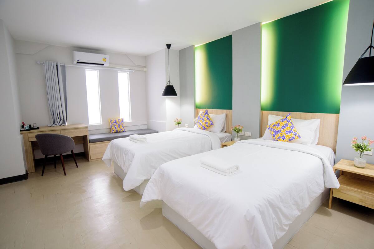 A hotel room with two beds, a desk, a chair, and a window.