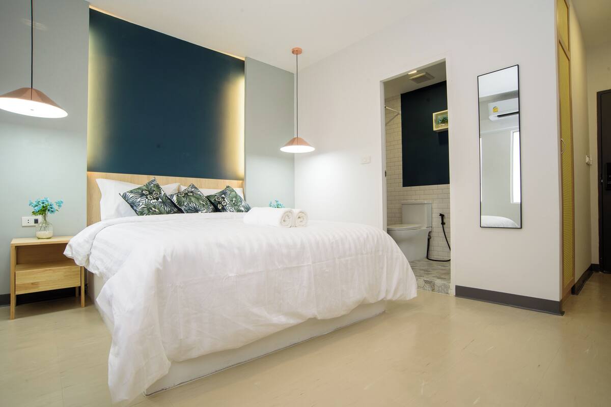 A modern bedroom with a large bed, bedside tables, a mirror, and a view into the bathroom.