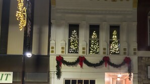 Een gebouw met twee verdiepingen, versierd voor kerst, inclusief kransen en guirlandes, en verlichte ramen.