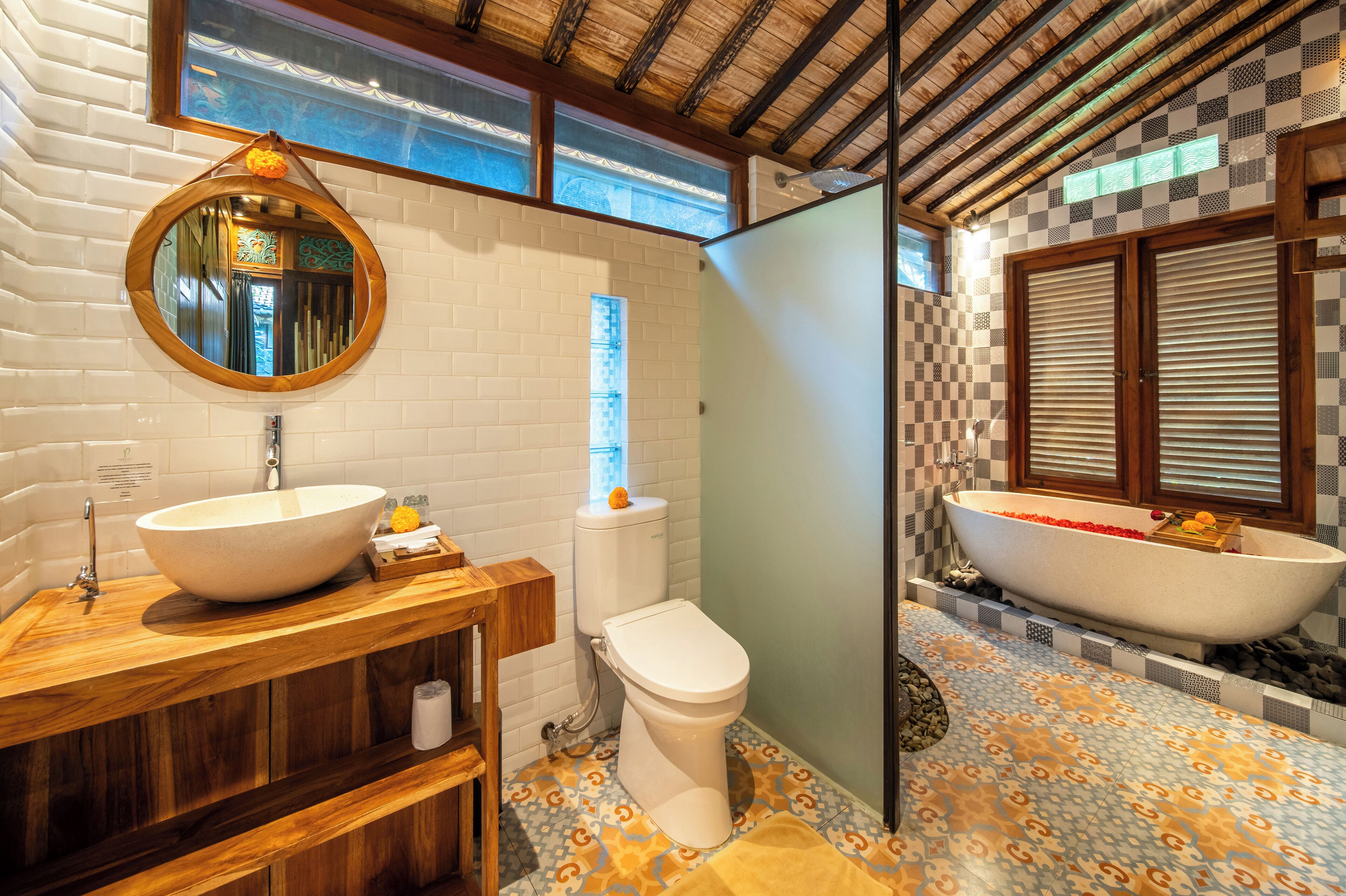 Een badkamer met een grote ronde spiegel, een houten wastafelmeubel, een toilet en een vrijstaand bad.