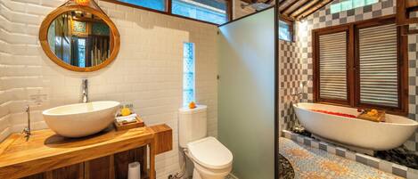A bathroom with a large round mirror, a wooden vanity, a toilet, and a freestanding bathtub.
