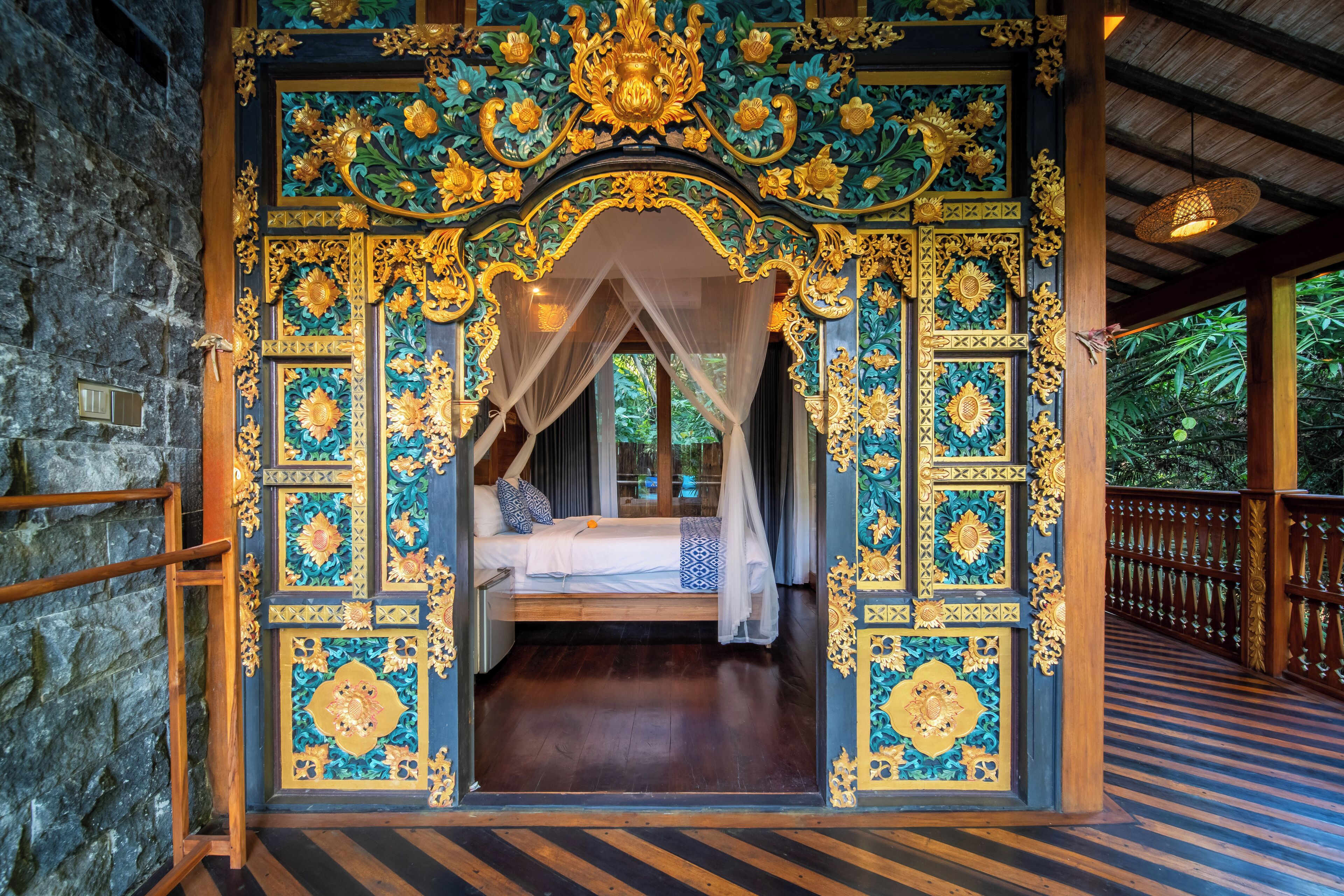 A room with a bed, ornate ceiling, and a stone wall.