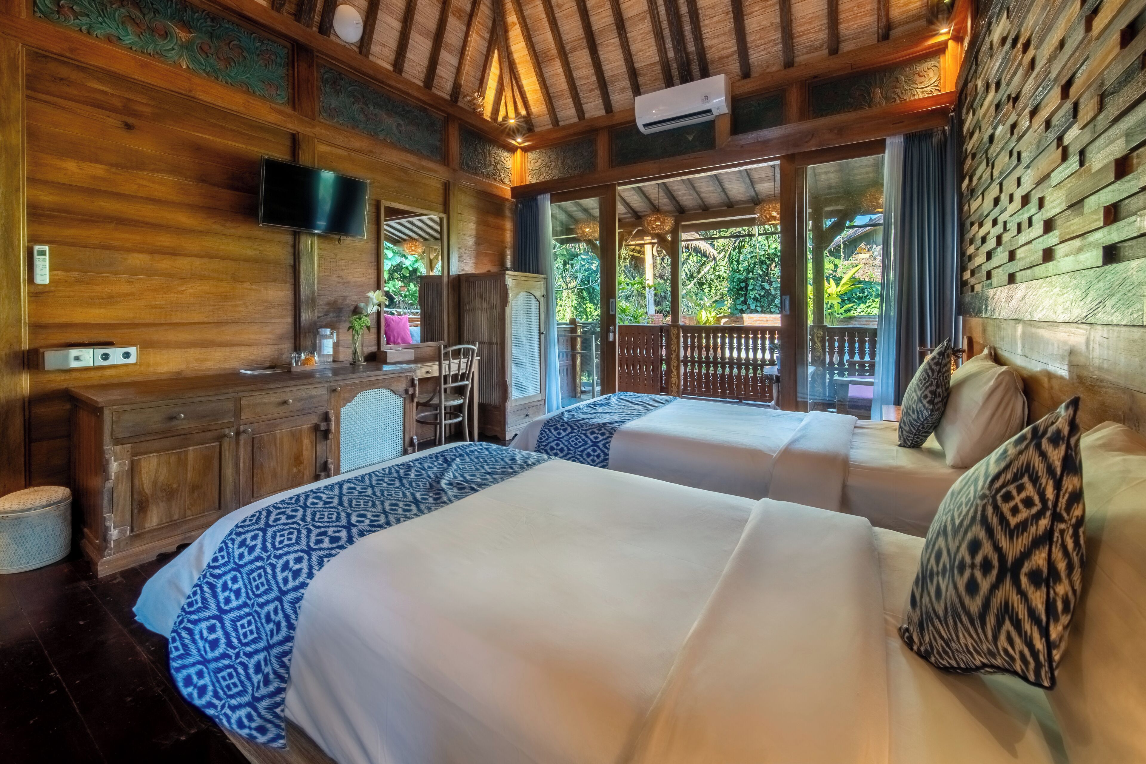 A room with two beds, a desk, a TV, and a large window with a view of greenery.