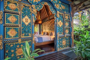 Een kamer met een bed, houten plafond en gedetailleerde blauwe en gouden wanddecoraties.