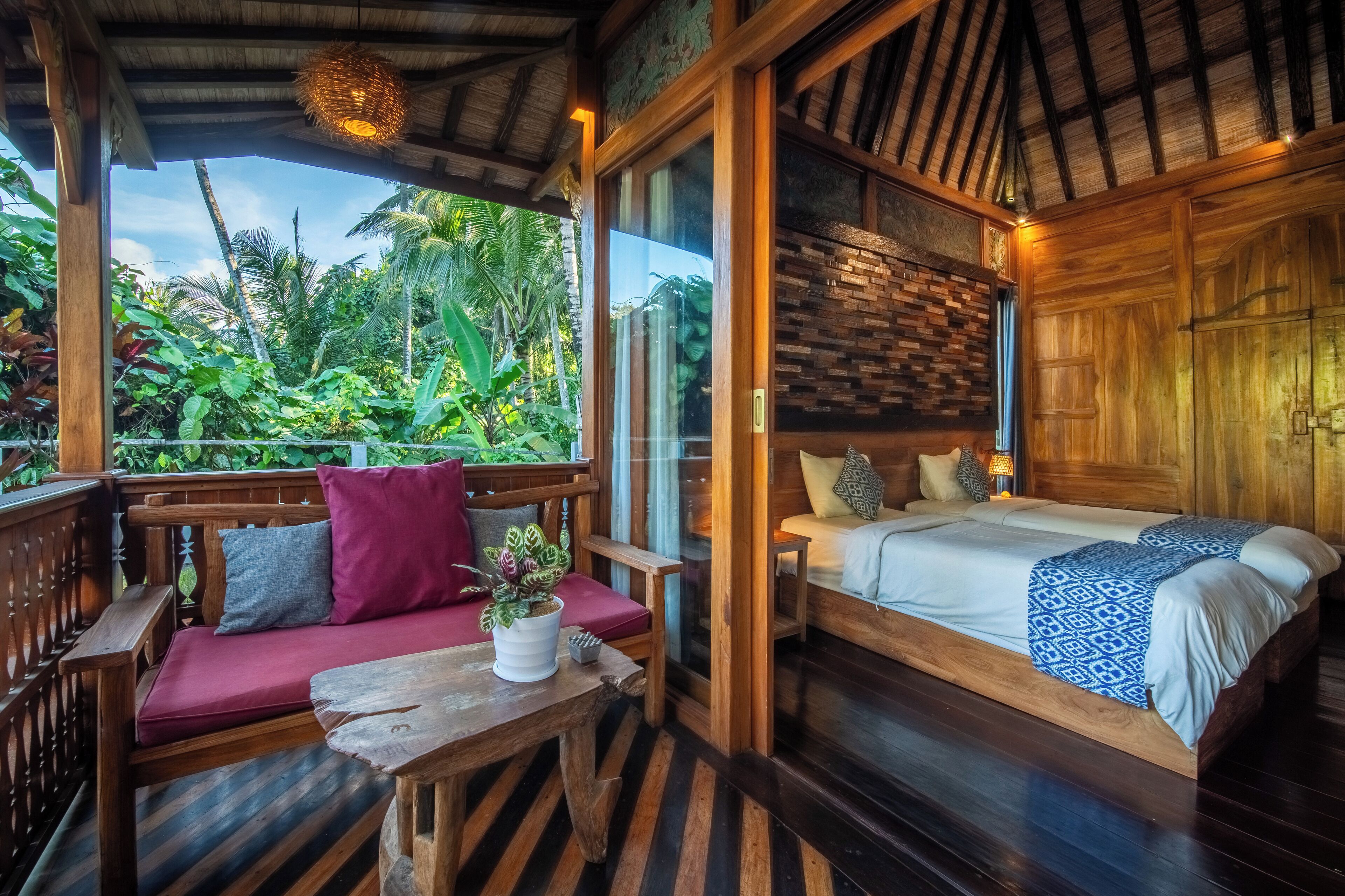 A wooden room with a bed, a sofa, and a table. There is a window with a view of greenery outside.