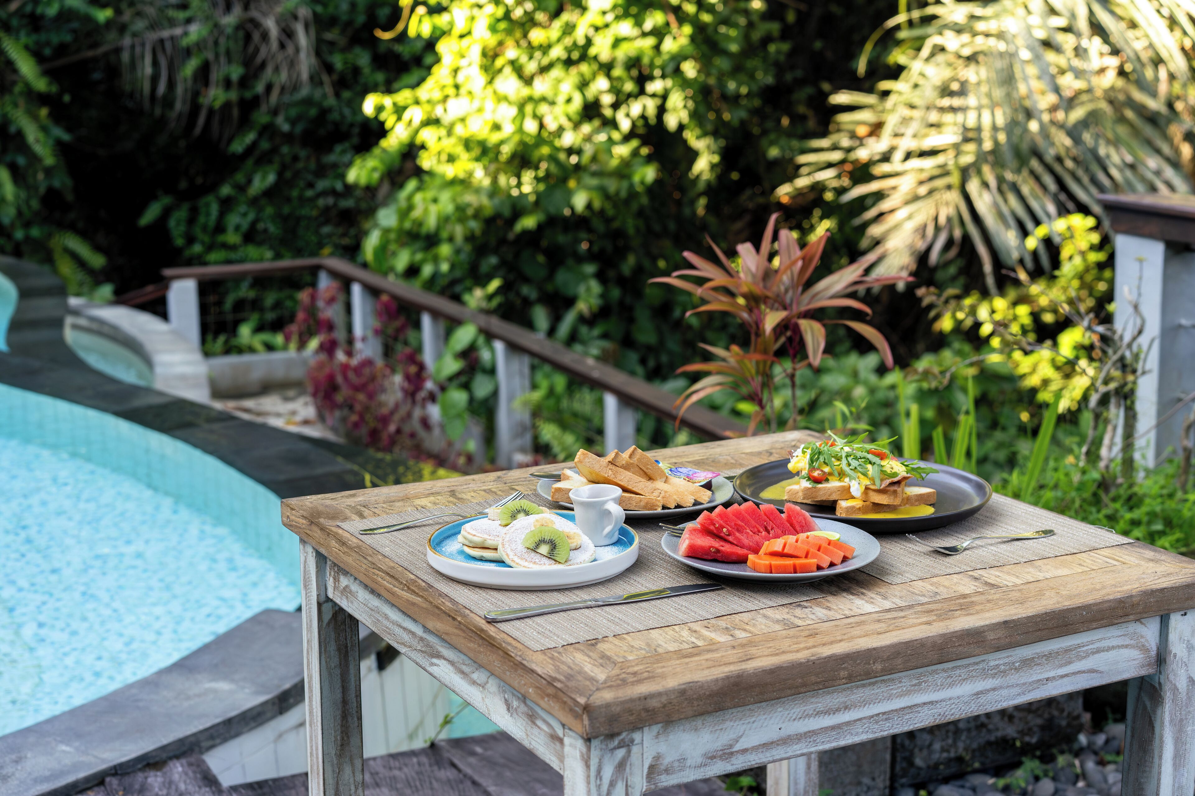 A wooden table with plates of food and a pool in the background.