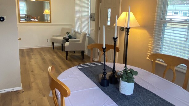 Ein Essbereich mit Tisch für vier Personen, zwei Kerzen, einem Blumentopf und Blick auf das angrenzende Wohnzimmer.