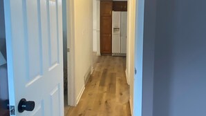 Ein Korridor mit Holzboden, weißen Wänden und einer Tür zu einer Küche.
