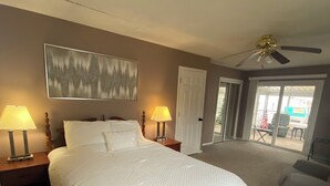 Ein Schlafzimmer mit einem großen Bett, zwei Nachttischlampen, einem Deckenventilator und Blick ins Freie durch eine Glastür.