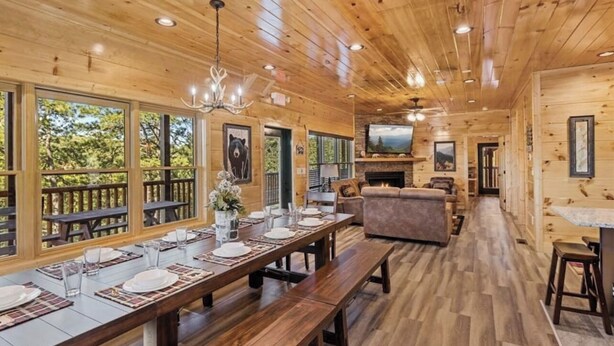 A wooden cabin interior with a dining area, sofa, TV, and fireplace.