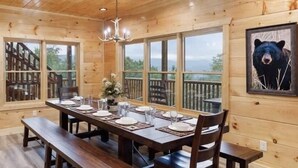 A wooden cabin dining room with a large table set for four, benches, and a chandelier.