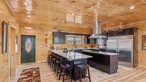 A modern kitchen with wooden walls, a central island with bar stools, stainless steel appliances, and a large window.