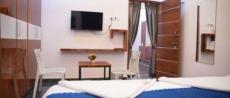 A hotel room with a bed, a TV, a desk with a chair, and a wardrobe.