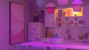 Een keuken met een wit aanrecht, een witte koelkast en een witte spoelbak. Er staan witte stoelen rond de tafel, en een witte vaas met bloemen op het aanrecht.