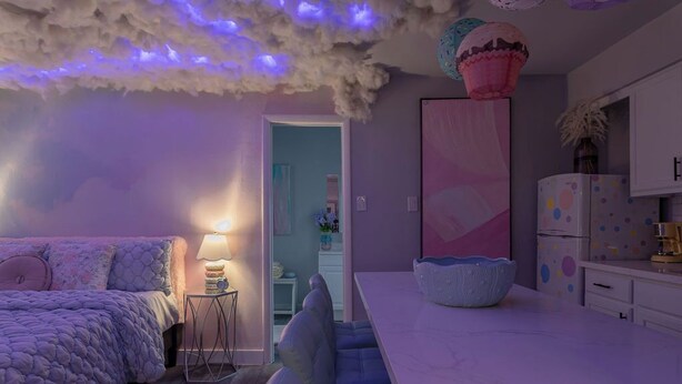 Een moderne slaapkamer met een bed, nachtkastje en lamp. Er is een deur naar een andere kamer.