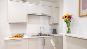 Una cocina moderna con armarios blancos, un fregadero y una encimera con una cafetera y un jarrón de flores.
