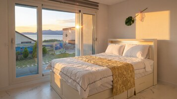 A bedroom with a bed, a large window, and a view of a building and landscape.