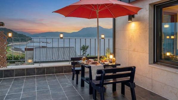 A terrace with a table set for dining, a red umbrella, and a view of a body of water and mountains. - That Day's Namhae Ocean View Pension (Namhae)