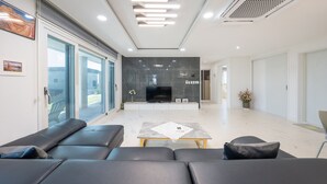 Una sala de estar moderna con un televisor grande, un sofá de cuero negro y un ventanal que da a un balcón.