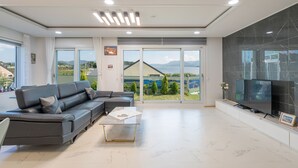 Una sala de estar moderna con un sofá modular, un televisor de pantalla plana y un amplio ventanal corredero que da a un balcón con vistas al mar y las montañas.