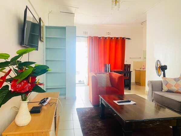A living room with a sofa, a coffee table, a TV mounted on the wall, and a plant. - Lux Suites Villa Reese Kisumu (Kisumu)