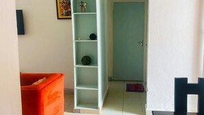 Ett rum med ett vitt kaklat golv, en röd soffa, en vit hylla, ett svart bord och en dörr som leder till ett annat rum.