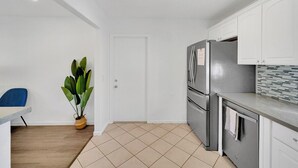 Eine moderne Küche mit weißen Schränken, einem Edelstahlkühlschrank und einer gefliesten Spritzschutzwand.