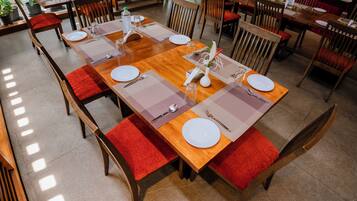A dining area with wooden tables, red cushioned chairs, and neatly set tables with plates, cutlery, and glasses.
