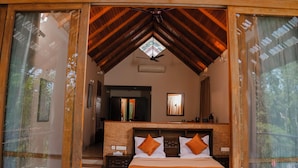 A bedroom with a wooden ceiling, a bed with pillows, and a view through a glass door.