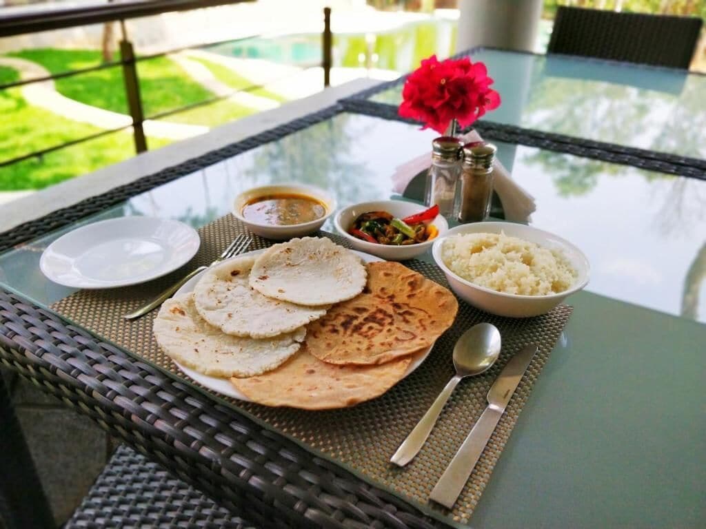 A table set with flatbreads, rice, curry, and a flower.