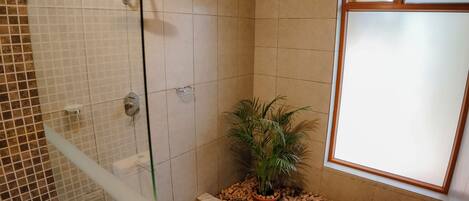 A bathroom with a glass shower enclosure, a potted plant, and a window with frosted glass.
