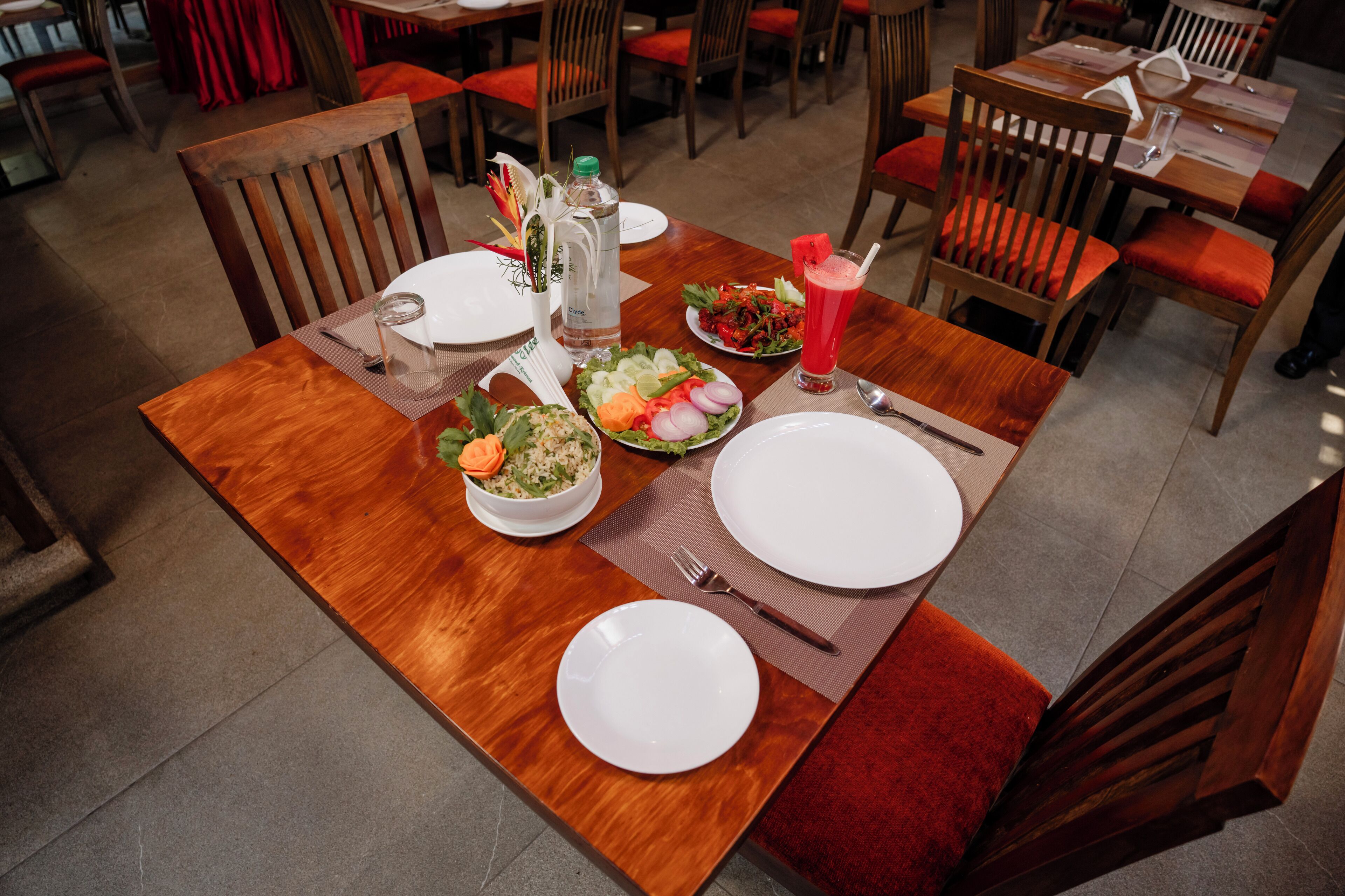A dining table set with plates, cutlery, a salad, a fruit drink, and condiments.
