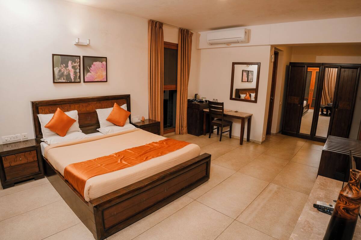 Une chambre d’hôtel avec un grand lit, un bureau et une chaise. Il y a un miroir au mur et une fenêtre avec des rideaux.