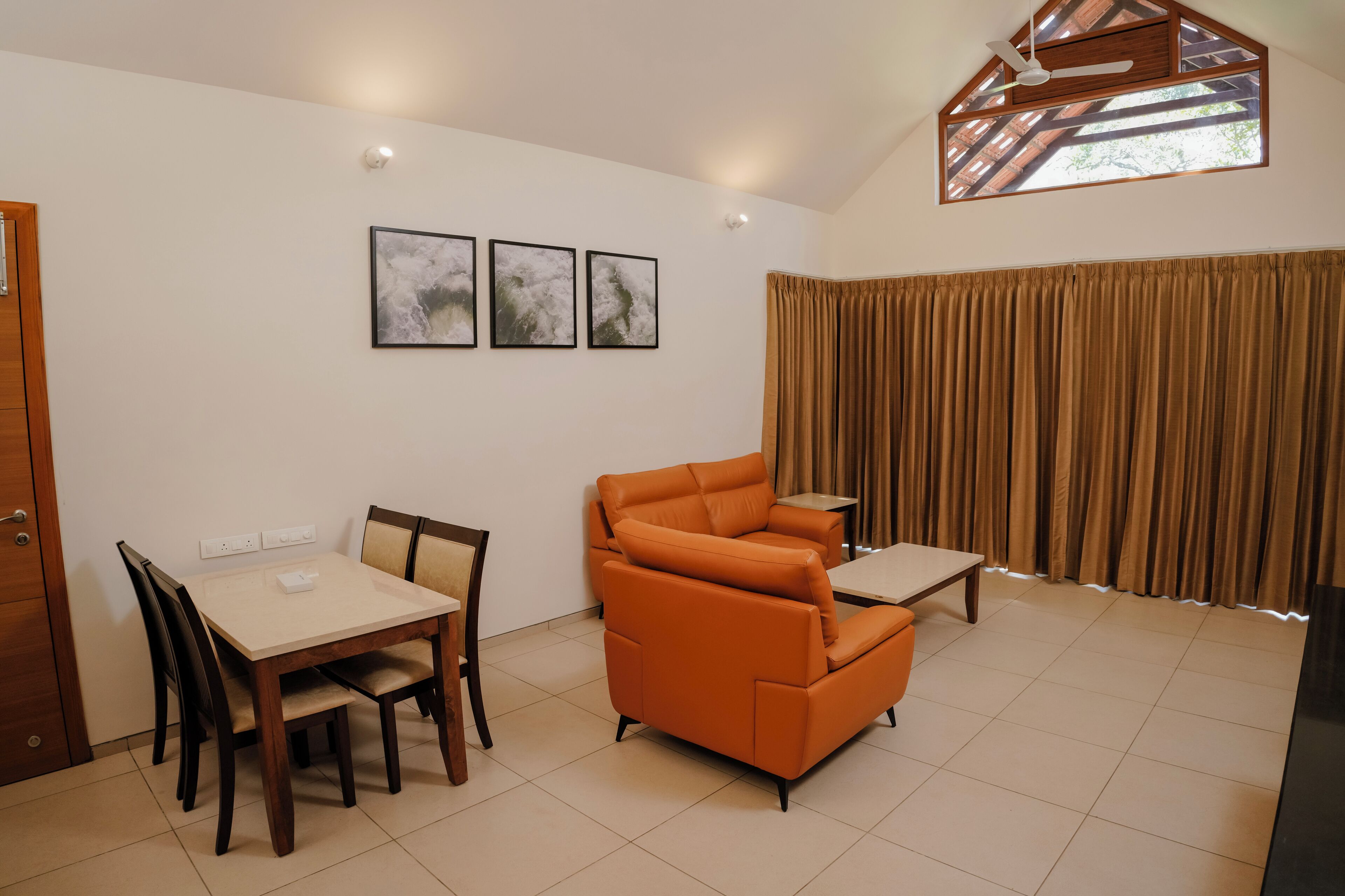 A living room with a dining table, chairs, an orange sofa, a small table, and a window with curtains.