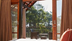 A bedroom with a large sliding glass door leading to a balcony with wicker furniture and a view of trees.