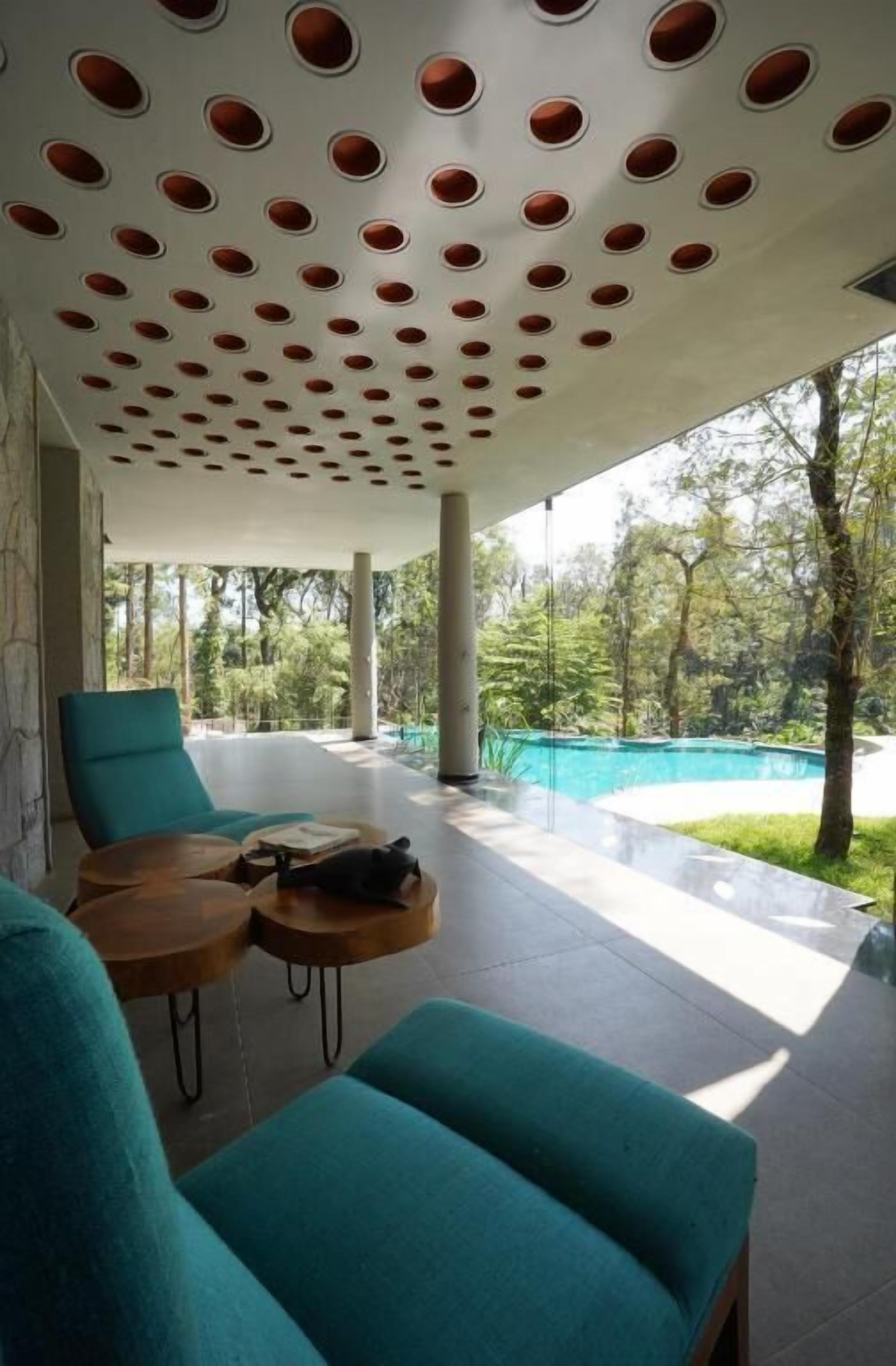 A modern outdoor seating area with teal chairs and a wooden table, overlooking a swimming pool and lush greenery.